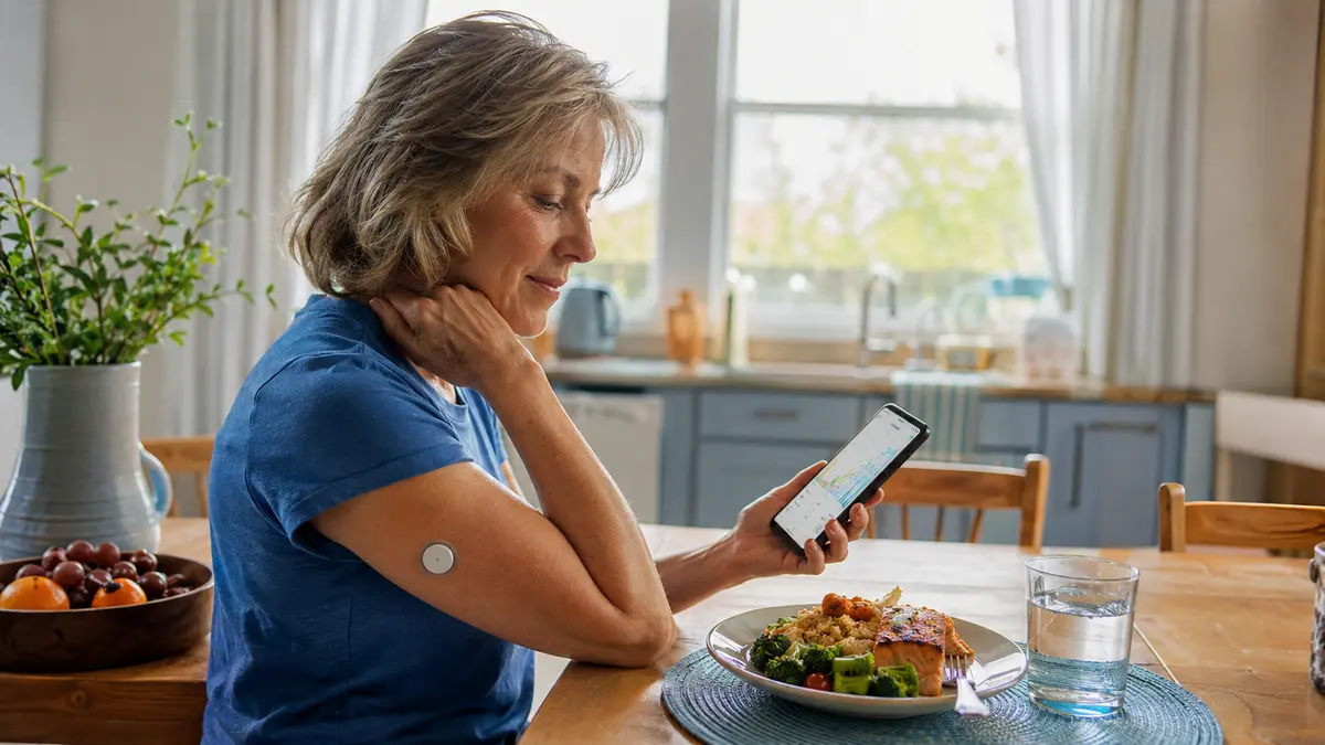 A woman reviewing glucose patterns on her phone while wearing a continuous glucose monitor.